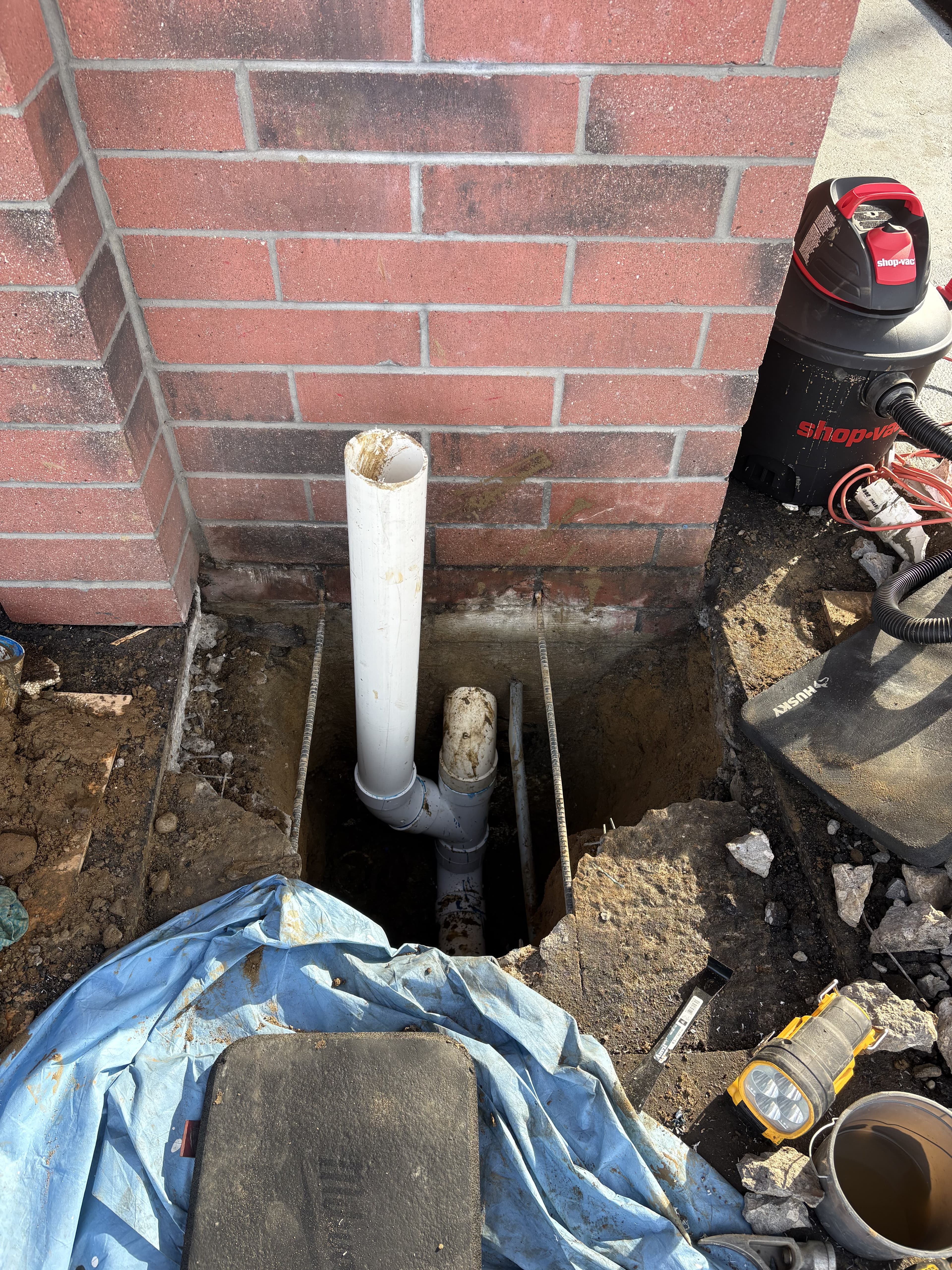 Drainage repair area opened beside a brick wall before the permanent finish was restored.